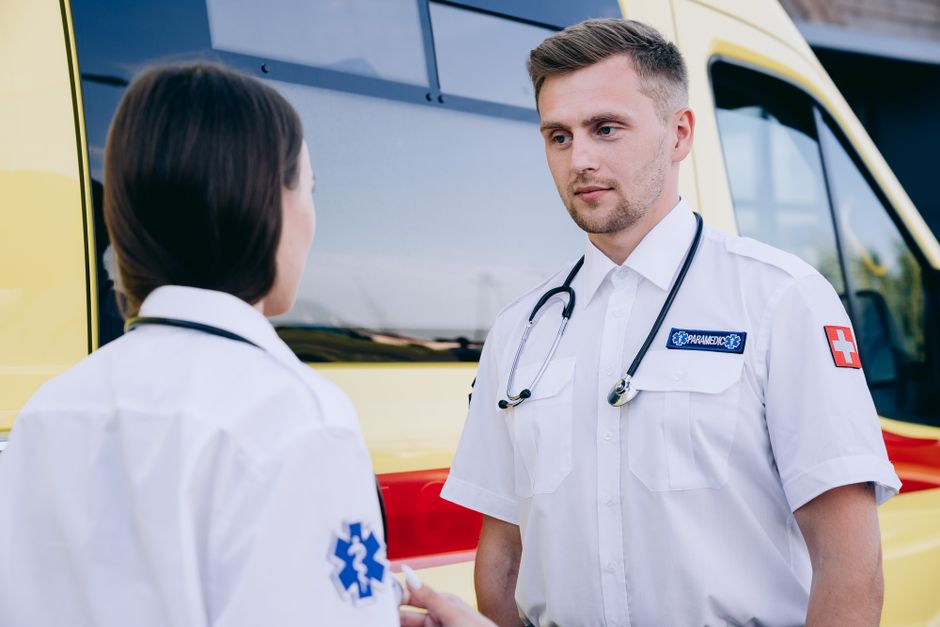 Two paramedics in uniform discussing beside an ambulance during daytime.